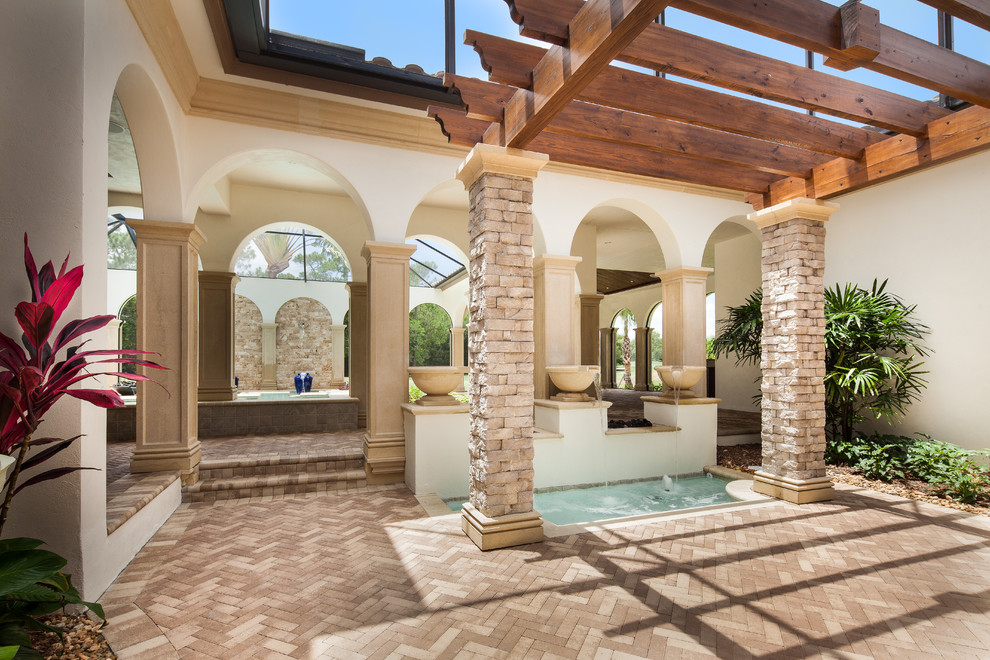 This is an example of a mid-sized mediterranean backyard patio in Miami with a water feature, natural stone pavers and a pergola.