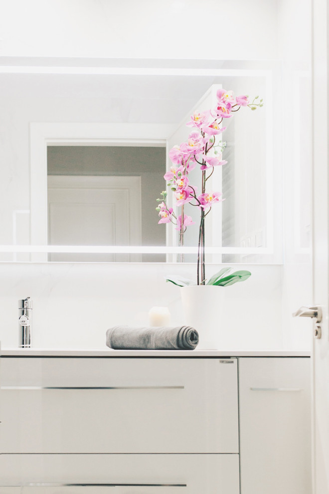 Photo of a traditional powder room in Other with flat-panel cabinets, white cabinets, a two-piece toilet, white tile, marble, white walls, marble floors, an undermount sink, engineered quartz benchtops and white floor.