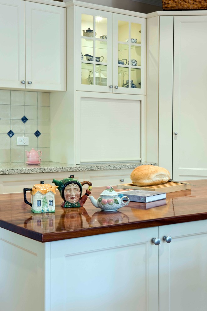 Mid-sized traditional l-shaped eat-in kitchen in Melbourne with a farmhouse sink, recessed-panel cabinets, white cabinets, wood benchtops, white splashback, terra-cotta splashback, stainless steel appliances, light hardwood floors and with island.