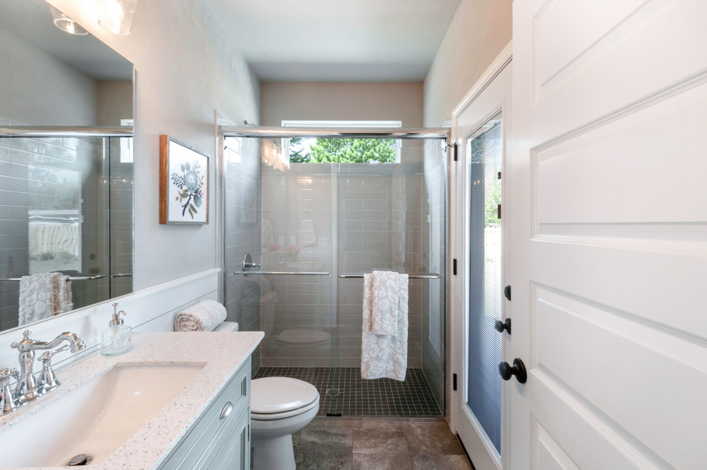 Inspiration for a mid-sized country kids bathroom with flat-panel cabinets, turquoise cabinets, an open shower, a one-piece toilet, grey walls, porcelain floors, a vessel sink, granite benchtops, grey floor, a sliding shower screen and white benchtops.