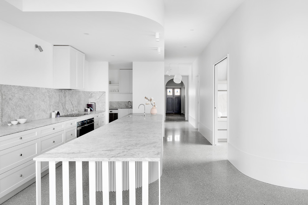 This is an example of a large contemporary galley open plan kitchen in Melbourne with shaker cabinets, grey splashback, concrete floors, with island and grey benchtop.