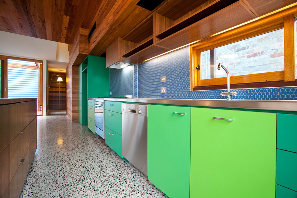 Photo of a mid-sized contemporary single-wall eat-in kitchen in Melbourne with an integrated sink, flat-panel cabinets, stainless steel benchtops, blue splashback, mosaic tile splashback, stainless steel appliances, concrete floors, with island and green cabinets.