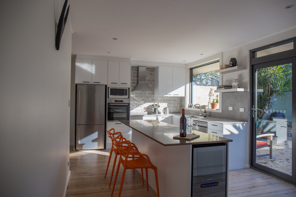 This is an example of a mid-sized scandinavian l-shaped eat-in kitchen in Sydney with a double-bowl sink, flat-panel cabinets, white cabinets, quartz benchtops, grey splashback, ceramic splashback, stainless steel appliances, light hardwood floors, with island, white floor, brown benchtop and coffered.