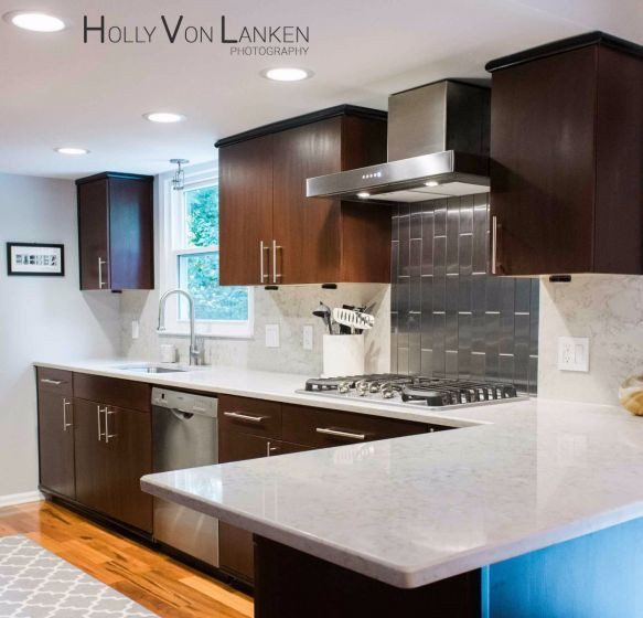 This is an example of a modern kitchen/diner in Indianapolis with metal splashback, stainless steel appliances, white worktops, flat-panel cabinets, dark wood cabinets, light hardwood flooring and metallic splashback.