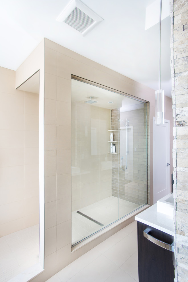 Photo of a large industrial master bathroom in Toronto with flat-panel cabinets, brown cabinets, a drop-in tub, an alcove shower, beige tile, brown tile, stone tile, beige walls, porcelain floors, a trough sink, engineered quartz benchtops, beige floor and a hinged shower door.