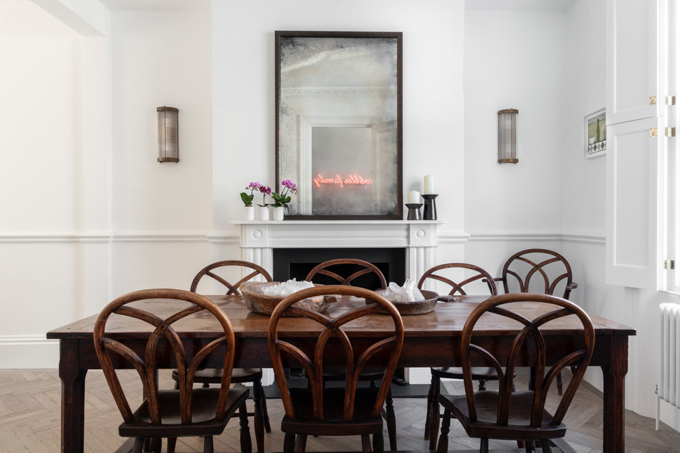Photo of a mid-sized contemporary dining room in London with white walls, light hardwood floors, a standard fireplace, a metal fireplace surround and grey floor.