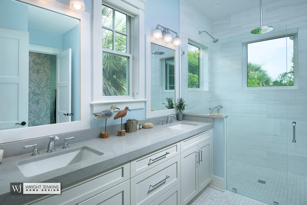 Design ideas for a mid-sized beach style master bathroom in Tampa with flat-panel cabinets, white cabinets, a curbless shower, a one-piece toilet, white tile, stone slab, blue walls, light hardwood floors, an undermount sink, marble benchtops, beige floor, a hinged shower door and grey benchtops.