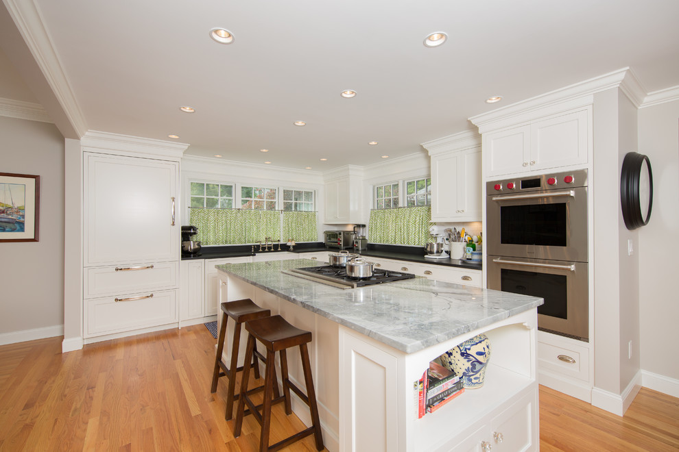 Kitchen - transitional medium tone wood floor kitchen idea in Boston with a farmhouse sink, recessed-panel cabinets, white cabinets, granite countertops, white backsplash, subway tile backsplash, stainless steel appliances and two islands