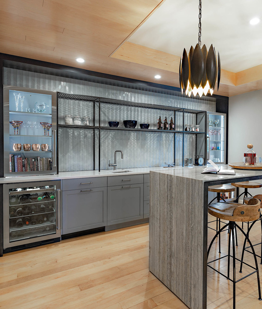 Design ideas for a large modern single-wall seated home bar in Other with an undermount sink, recessed-panel cabinets, light hardwood floors, brown floor, grey benchtop, grey cabinets, grey splashback and glass tile splashback.