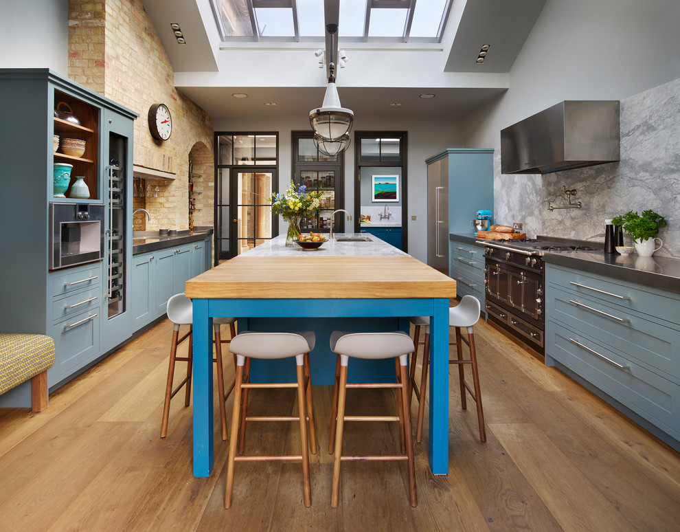 Photo of a large transitional u-shaped separate kitchen in London with an undermount sink, recessed-panel cabinets, blue cabinets, grey splashback, stone slab splashback, stainless steel appliances, medium hardwood floors, with island, brown floor and quartzite benchtops.
