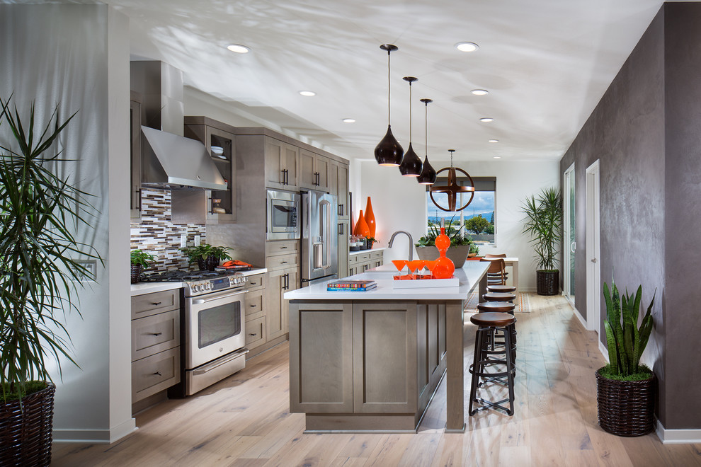 Photo of a beach style single-wall kitchen in Orange County with a farmhouse sink, shaker cabinets, grey cabinets, multi-coloured splashback, stainless steel appliances, medium hardwood floors and with island.