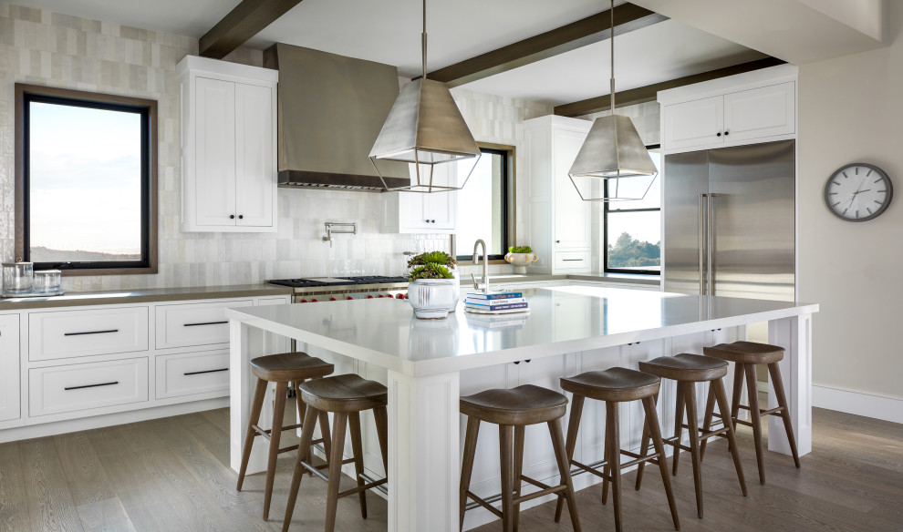 Inspiration for a large transitional u-shaped eat-in kitchen in Los Angeles with a farmhouse sink, recessed-panel cabinets, white cabinets, quartzite benchtops, white splashback, ceramic splashback, stainless steel appliances, light hardwood floors, with island, grey floor and white benchtop.