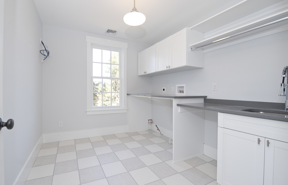 Photo of a mid-sized traditional single-wall dedicated laundry room in Philadelphia with a single-bowl sink, flat-panel cabinets, white cabinets, granite benchtops, grey walls, light hardwood floors and a side-by-side washer and dryer.