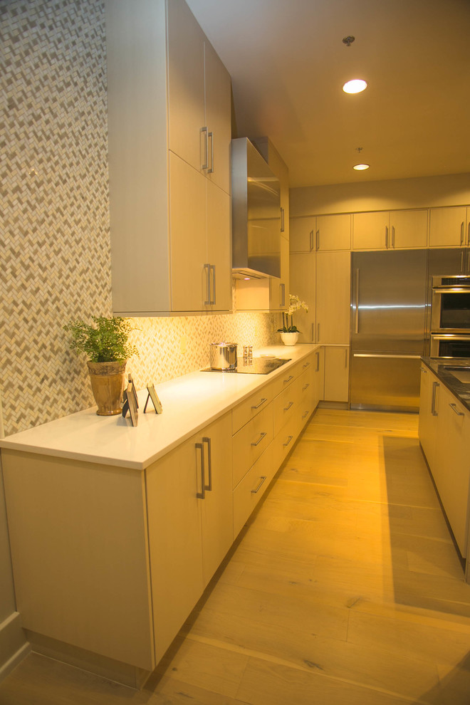 Inspiration for a mid-sized transitional l-shaped light wood floor kitchen remodel in New Orleans with an undermount sink, flat-panel cabinets, beige cabinets, multicolored backsplash, mosaic tile backsplash, stainless steel appliances and an island