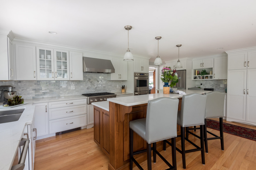 Eat-in kitchen - large transitional l-shaped medium tone wood floor, brown floor and coffered ceiling eat-in kitchen idea in Boston with an undermount sink, shaker cabinets, white cabinets, quartz countertops, gray backsplash, subway tile backsplash, stainless steel appliances, an island and white countertops