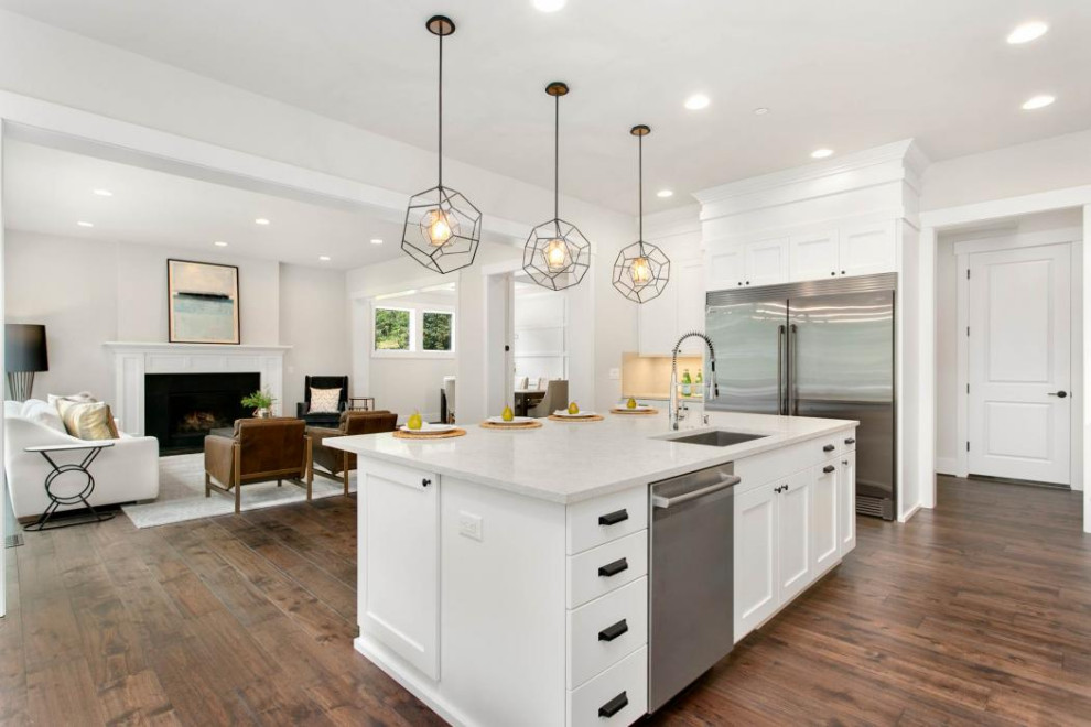 Large contemporary u-shaped open plan kitchen in Seattle with a drop-in sink, shaker cabinets, white cabinets, quartz benchtops, beige splashback, cement tile splashback, stainless steel appliances, dark hardwood floors, with island, brown floor and white benchtop.