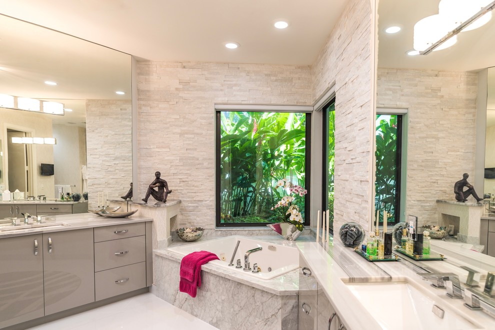 Inspiration for a large contemporary master bathroom in Miami with flat-panel cabinets, grey cabinets, a corner tub, a corner shower, a one-piece toilet, white tile, stone slab, grey walls, ceramic floors, an undermount sink and marble benchtops.
