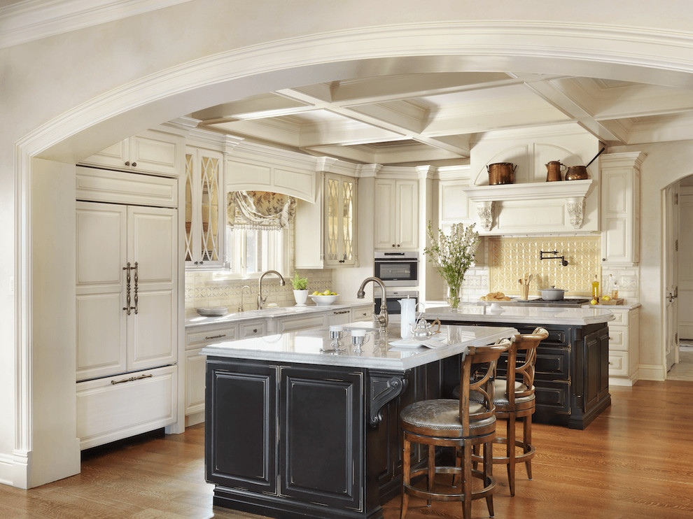Photo of a traditional kitchen in St Louis with raised-panel cabinets, beige cabinets, quartzite benchtops, beige splashback, stainless steel appliances, medium hardwood floors and multiple islands.