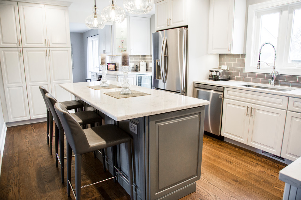 Eat-in kitchen - mid-sized transitional l-shaped medium tone wood floor and brown floor eat-in kitchen idea in Chicago with an undermount sink, raised-panel cabinets, white cabinets, quartz countertops, gray backsplash, ceramic backsplash, stainless steel appliances, an island and white countertops