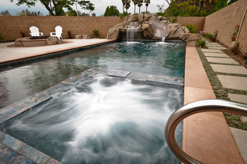 Photo of a mid-sized tropical backyard rectangular lap pool in Los Angeles with a water slide and concrete slab.
