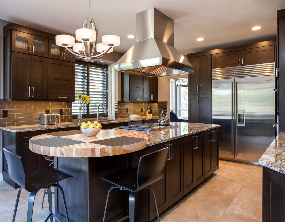 This is an example of an expansive arts and crafts u-shaped open plan kitchen in Denver with an undermount sink, shaker cabinets, dark wood cabinets, granite benchtops, brown splashback, glass tile splashback, stainless steel appliances, ceramic floors and with island.