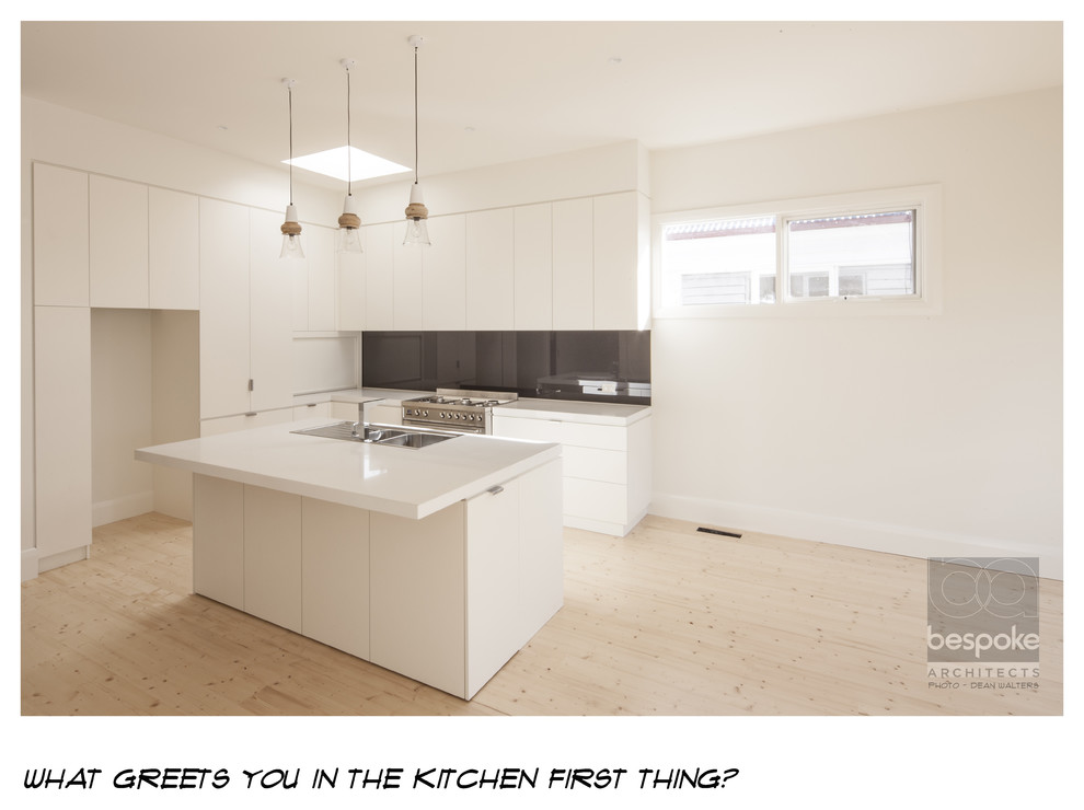 Mid-sized contemporary l-shaped open plan kitchen in Geelong with a double-bowl sink, flat-panel cabinets, white cabinets, quartz benchtops, glass sheet splashback, stainless steel appliances, light hardwood floors, with island and black splashback.