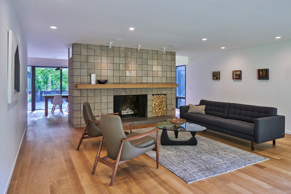 Midcentury living room in Grand Rapids with white walls, light hardwood floors, a standard fireplace, a tile fireplace surround and beige floor.
