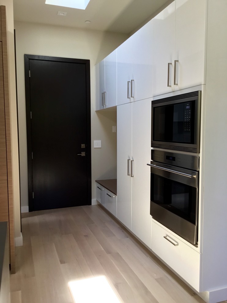 Photo of a large contemporary u-shaped separate kitchen in San Francisco with flat-panel cabinets, white cabinets, stainless steel appliances, light hardwood floors and with island.