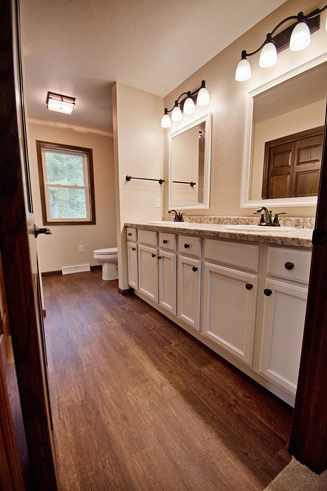 Mid-sized transitional medium tone wood floor and brown floor bathroom photo with recessed-panel cabinets, white cabinets, a one-piece toilet, beige walls, a drop-in sink, laminate countertops and beige countertops