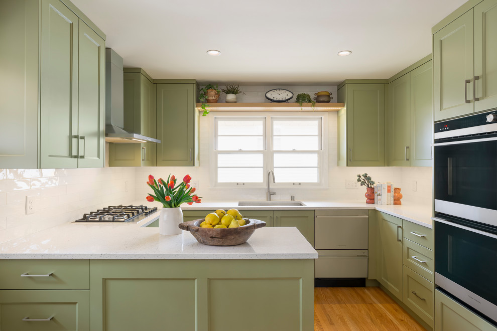 Small midcentury u-shaped eat-in kitchen in Minneapolis with a double-bowl sink, recessed-panel cabinets, green cabinets, quartz benchtops, white splashback, ceramic splashback, stainless steel appliances, light hardwood floors, no island, brown floor and white benchtop.