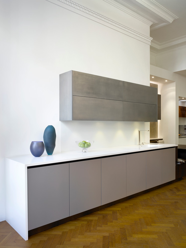 This is an example of a large contemporary open plan kitchen in London with an integrated sink, flat-panel cabinets, solid surface benchtops and white splashback.