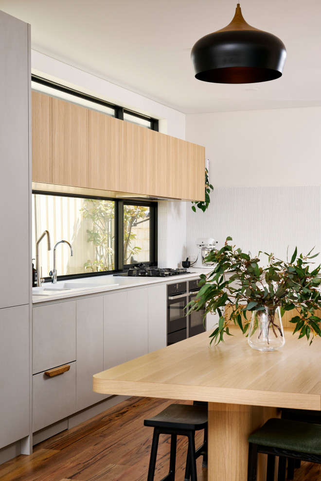 Large scandinavian galley open plan kitchen in Perth with a double-bowl sink, flat-panel cabinets, grey cabinets, quartz benchtops, white splashback, mosaic tile splashback, black appliances, medium hardwood floors, with island, brown floor and white benchtop.