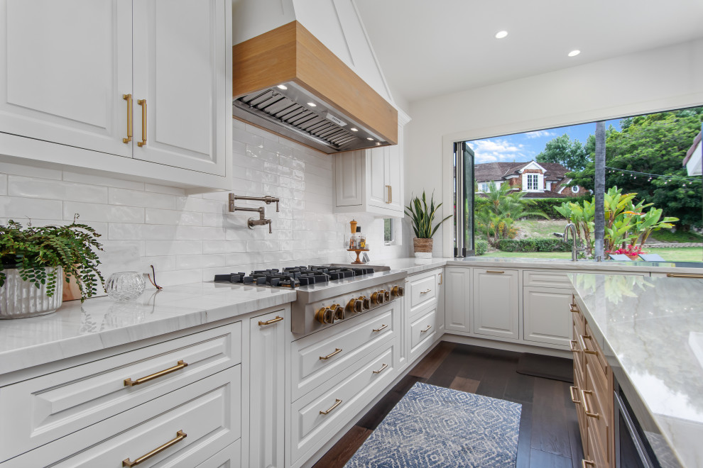 Inspiration for a large transitional l-shaped dark wood floor and brown floor open concept kitchen remodel in Orange County with an undermount sink, raised-panel cabinets, white cabinets, quartzite countertops, white backsplash, ceramic backsplash, stainless steel appliances, an island and white countertops