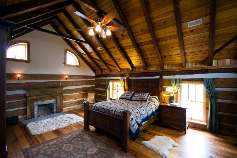 This is an example of a large country bedroom in Other with brown walls, light hardwood floors, a standard fireplace, a wood fireplace surround, vaulted and wood walls.