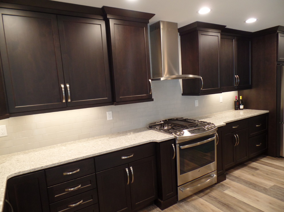 Inspiration for a large transitional l-shaped medium tone wood floor and beige floor eat-in kitchen remodel in Cedar Rapids with an undermount sink, shaker cabinets, dark wood cabinets, granite countertops, white backsplash, subway tile backsplash, stainless steel appliances and an island