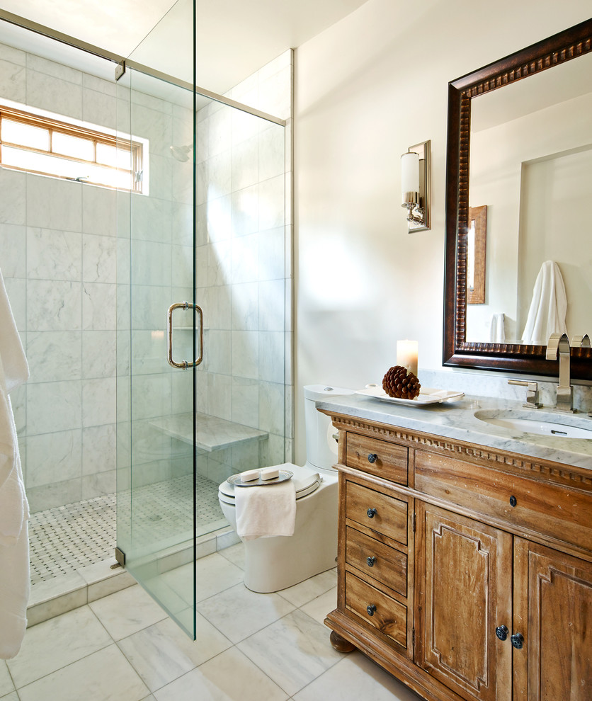Inspiration for a mid-sized country 3/4 bathroom in Other with an undermount sink, recessed-panel cabinets, an alcove shower, white tile, medium wood cabinets, a one-piece toilet, marble, white walls, marble floors, marble benchtops, white floor and a hinged shower door.