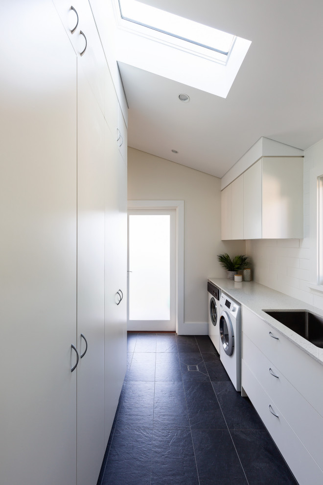 Foto di una sala lavanderia country di medie dimensioni con lavello sottopiano, ante lisce, ante bianche, top in quarzo composito, paraspruzzi bianco, paraspruzzi con piastrelle in ceramica, pareti bianche, pavimento con piastrelle in ceramica, lavatrice e asciugatrice affiancate, pavimento grigio e top bianco