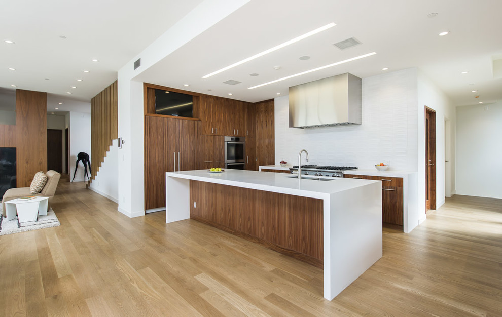 Contemporary u-shaped kitchen in Los Angeles with an undermount sink, flat-panel cabinets, dark wood cabinets, white splashback, stainless steel appliances, light hardwood floors and with island.