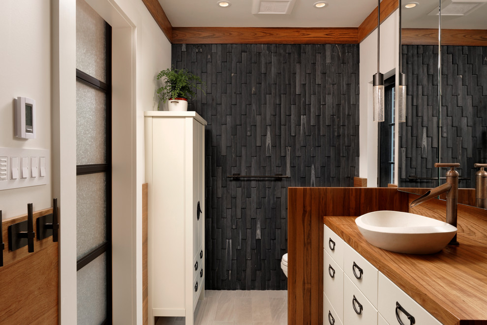 Mid-sized contemporary master bathroom in DC Metro with flat-panel cabinets, white cabinets, a drop-in tub, an open shower, a one-piece toilet, black tile, stone tile, white walls, a vessel sink, wood benchtops, white floor, vinyl floors and an open shower.