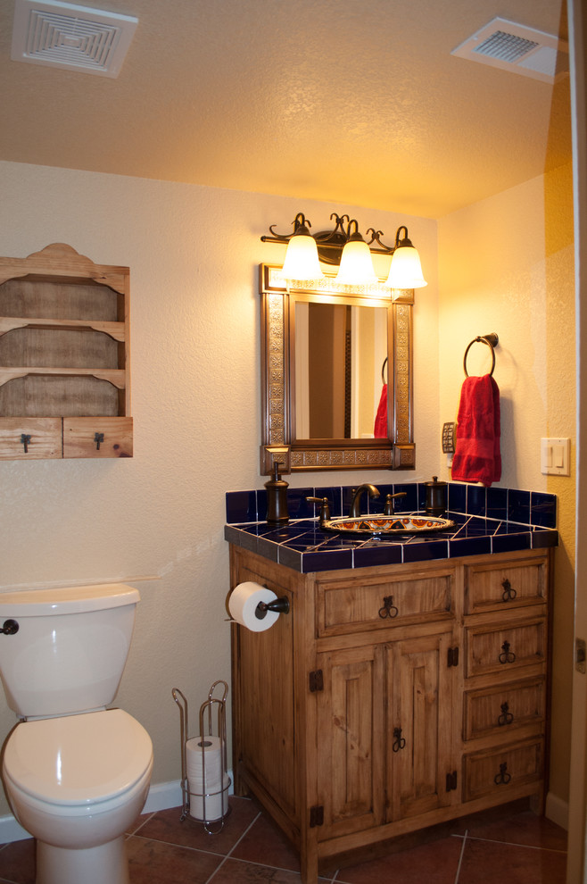 Inspiration for a mid-sized transitional master bathroom in Denver with recessed-panel cabinets, medium wood cabinets, an alcove shower, a two-piece toilet, blue tile, ceramic tile, beige walls, terra-cotta floors, a drop-in sink, tile benchtops, red floor, a hinged shower door and blue benchtops.