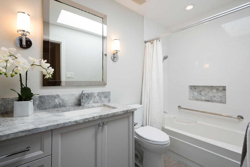 This is an example of a mid-sized transitional master bathroom in Vancouver with shaker cabinets, white cabinets, an alcove tub, a shower/bathtub combo, a two-piece toilet, white tile, porcelain tile, grey walls, porcelain floors, an undermount sink and marble benchtops.