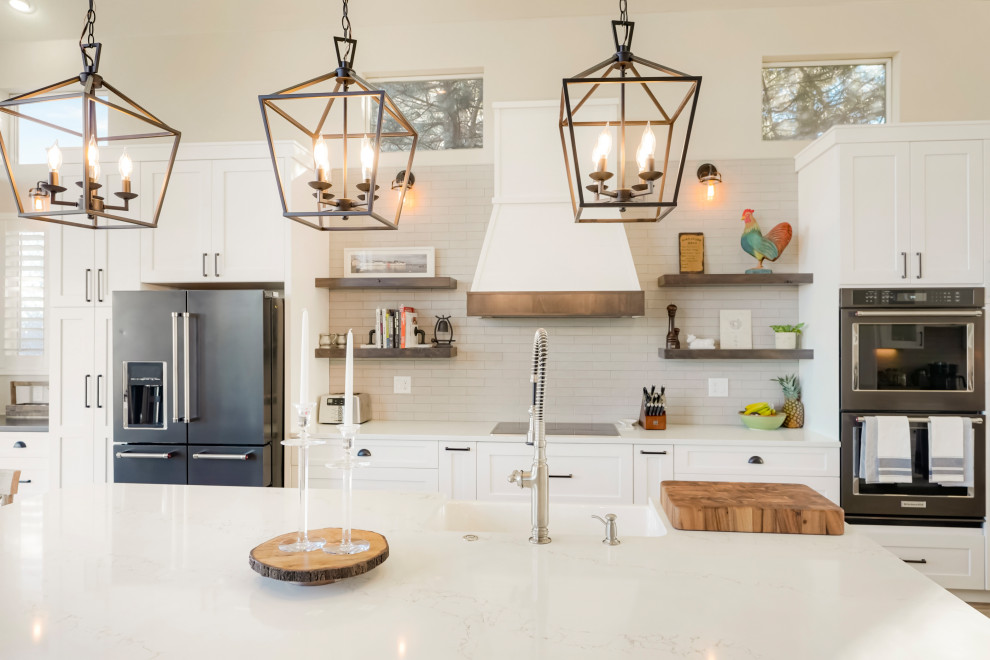 Open concept kitchen - large transitional single-wall vaulted ceiling open concept kitchen idea in Denver with a farmhouse sink, shaker cabinets, white cabinets, white backsplash, subway tile backsplash, black appliances, an island and white countertops
