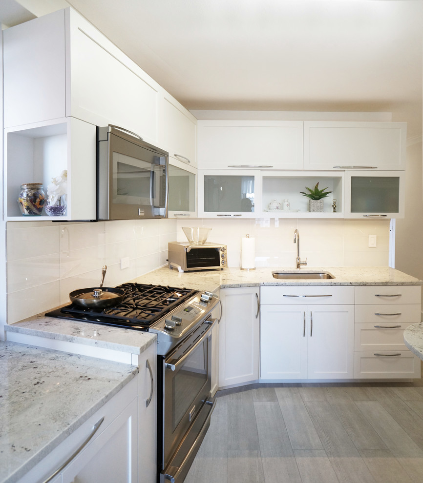 Contemporary separate kitchen in New York with an undermount sink, shaker cabinets, white cabinets, granite benchtops, white splashback, glass tile splashback, stainless steel appliances and porcelain floors.