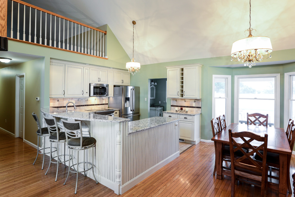 Example of a mid-sized transitional galley open concept kitchen design with a double-bowl sink, beaded inset cabinets, white cabinets, wood countertops, beige backsplash, ceramic backsplash, stainless steel appliances and a peninsula