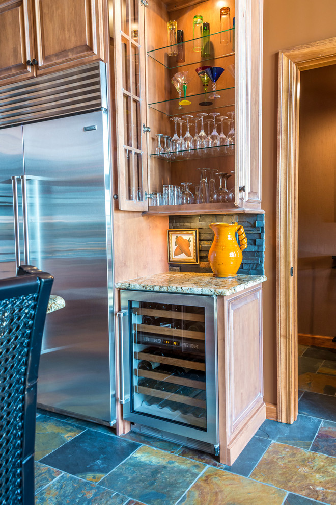 Small eclectic l-shaped slate floor open concept kitchen photo with an undermount sink, glass-front cabinets, light wood cabinets, granite countertops, black backsplash, stone tile backsplash, stainless steel appliances and an island