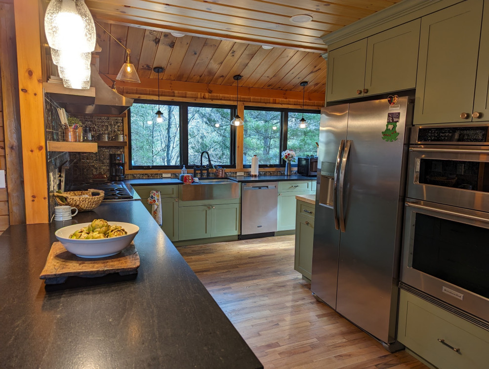 Example of a mid-sized mountain style l-shaped medium tone wood floor, brown floor and wood ceiling eat-in kitchen design with a farmhouse sink, shaker cabinets, green cabinets, granite countertops, multicolored backsplash, ceramic backsplash, stainless steel appliances and black countertops