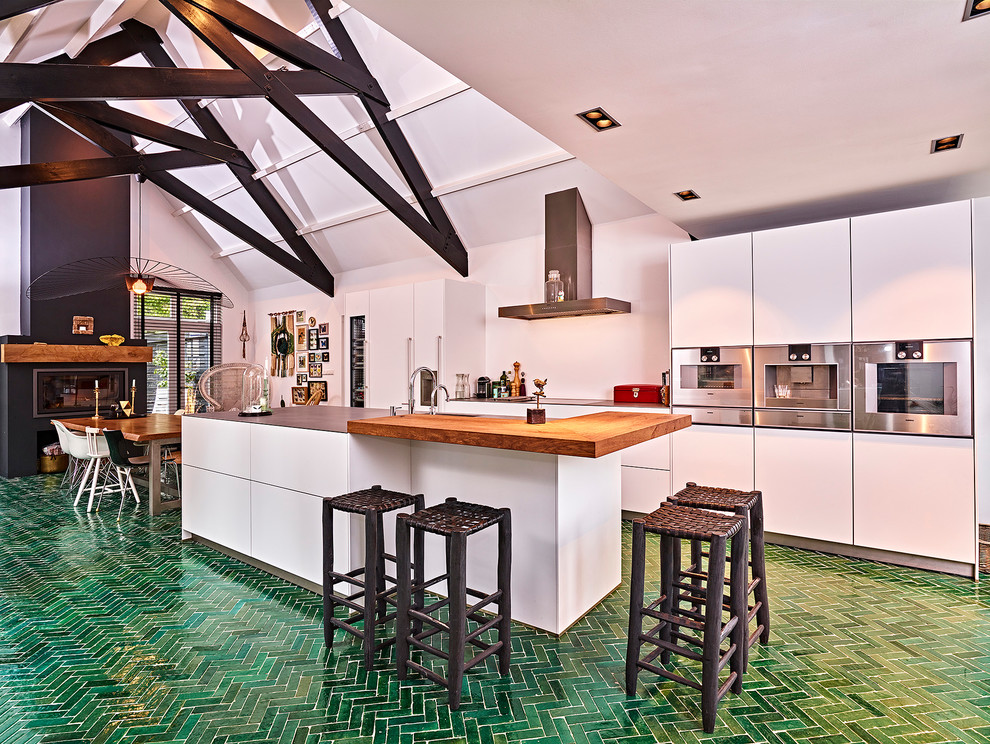 Photo of an expansive contemporary galley eat-in kitchen in Other with an integrated sink, flat-panel cabinets, white cabinets, stainless steel benchtops, white splashback, stainless steel appliances, ceramic floors, with island and green floor.