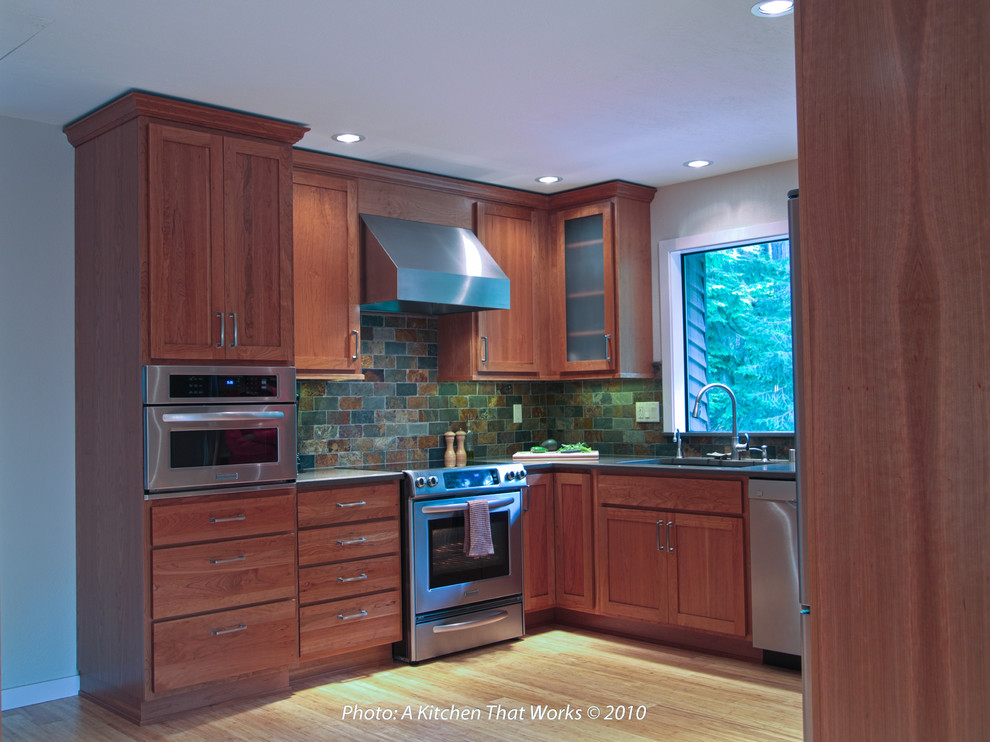 Photo of a mid-sized transitional u-shaped eat-in kitchen in Seattle with an undermount sink, recessed-panel cabinets, medium wood cabinets, quartz benchtops, green splashback, stone tile splashback, stainless steel appliances, bamboo floors, no island, beige floor and grey benchtop.