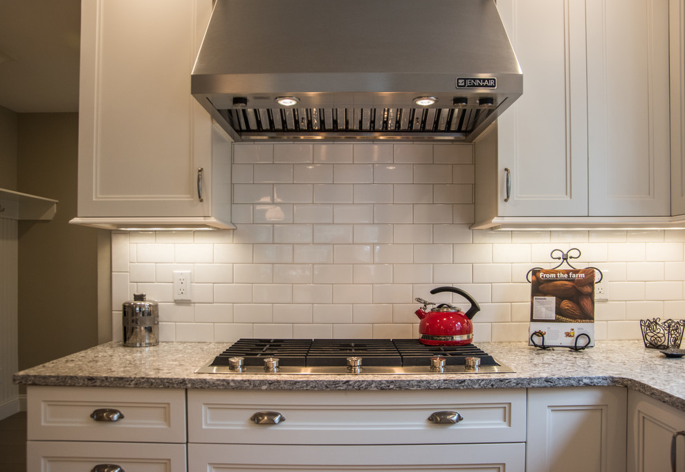Example of a mid-sized transitional l-shaped medium tone wood floor eat-in kitchen design in Boston with a farmhouse sink, shaker cabinets, white cabinets, quartz countertops, white backsplash, subway tile backsplash, stainless steel appliances and an island