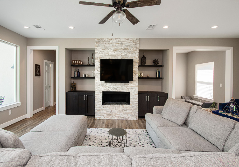 Inspiration for a mid-sized transitional open concept living room in Dallas with beige walls, vinyl floors, a hanging fireplace, a stone fireplace surround, a wall-mounted tv and brown floor.